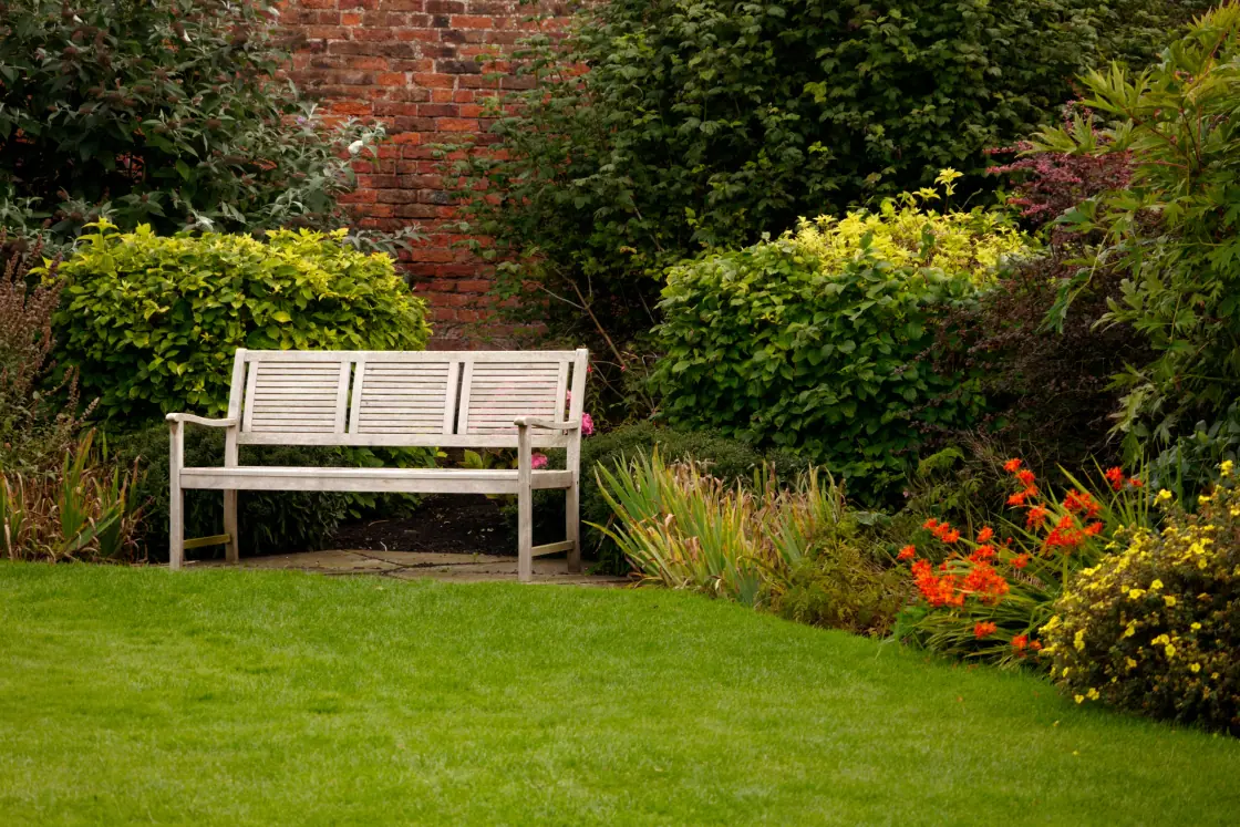 Gepflegter Garten mit Rasen, Bank und blühenden Beeten