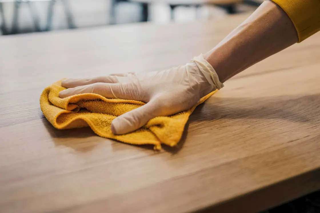 Behandschuhte Hand wischt mit einem gelben Mikrofasertuch eine Holzoberfläche
